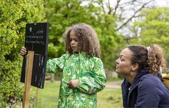 A child and parent looking at a trail sign in a garden.