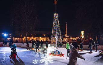 Ice rink lit up at night with festive lighting and christmas tree