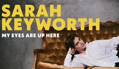 Sarah Keyworth laying on a sofa. On the left hand side there is a yellow text: Sarah Keyworth: My Eyes Are Up Here