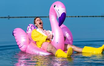 Harry baker sitting on a inflatable pool flamingo.