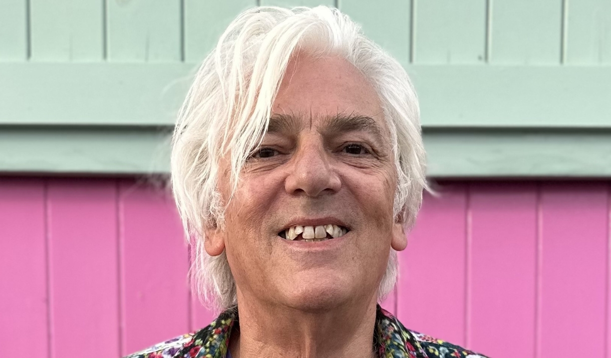 A man smiling towards the camera against a pink and white wall
