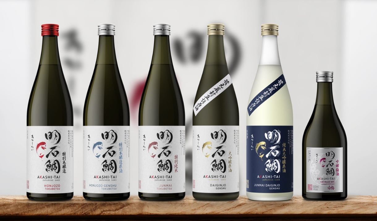 A picture of different sake bottles from Akash-Tai brewery in Japan lined up on a wooden board with a soft cream coloured background.