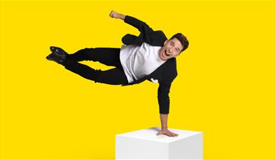 Man balancing with one hand on a yellow box
