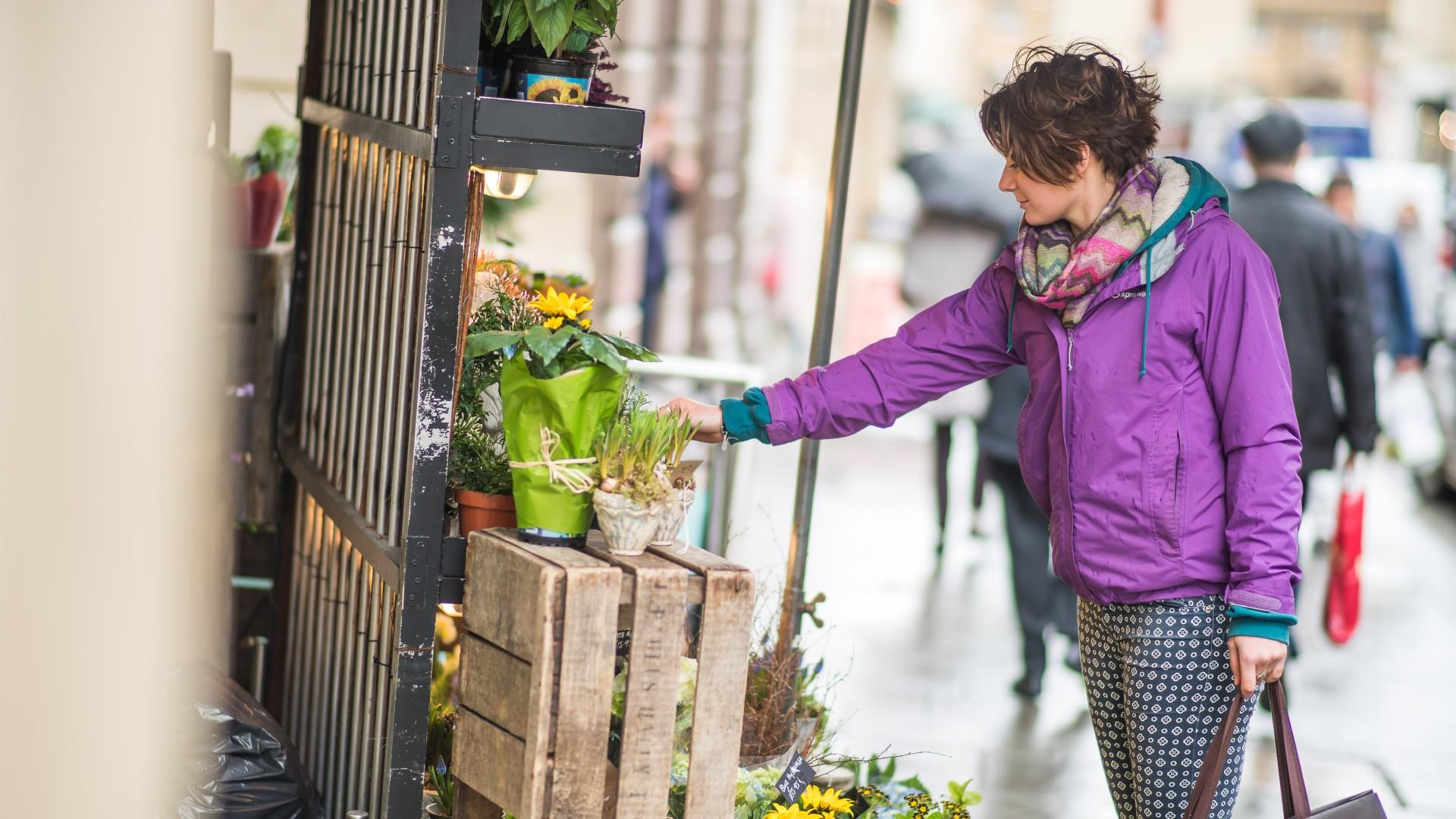 Woman in purple coat admires flowers outside of a shop