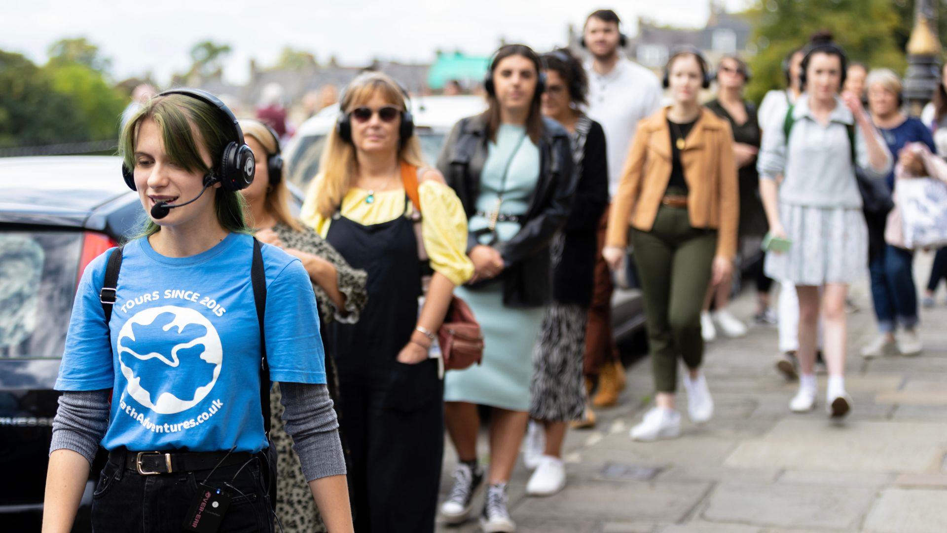 A group of people walking down a street in Bath city centre, led by a tour guide.