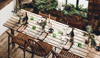 overhead shot of a beautiful bare brick warehouse space with a long table set for lunch and evergreens arranged on the large industrial window's sill