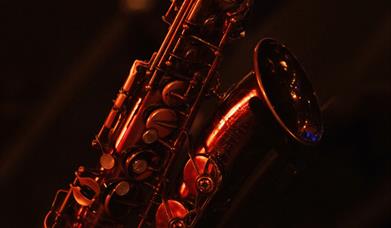 A saxophone bathed in warm red stage lighting against a dark background. 