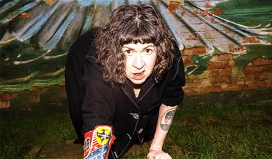 Amy Mason crawls towards the camera, she is on grass with a cowboy boot on her right arm