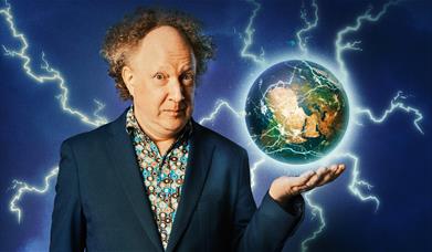 A photo of Andy Zaltzman, his holing a globe of the earth. Lighting is is shooting from the globe.  