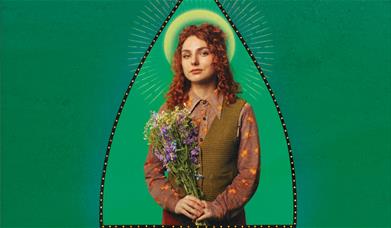  a Image on the comedian Ania Magliano - she is holing a bouquet of flowers against a green background.