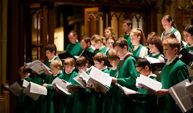 Boys in green choir robes hold sheet music and sing in a church