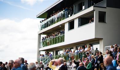 A crowd of spectators watching from the stands at Bath Racecourse