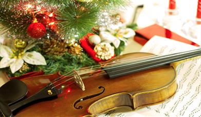 A violin surrounded by Christmas lights and ornaments