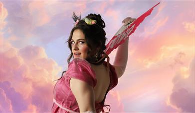 A woman in front of pink clouds, holds a fan, in 18th Century clothing.