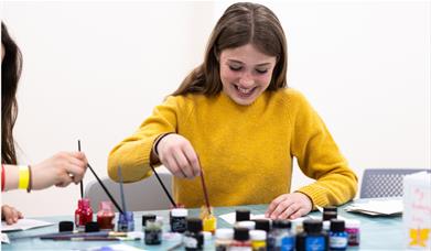 A girl wearing a bright yellow jumper creating an artwork with coloured inks