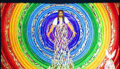 A brightly coloured embroidered panel of Jesus, surrounded by concentric circles of rainbow colours, with a crowd of people in front of Him