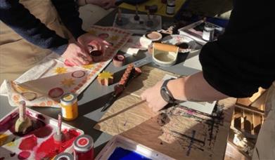 two women stand on opposite sides of a craft table, block printing and lino printing at the Love Makers Craft Cafe in Bath