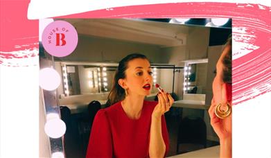 A woman doing her makeup in a dressing room. 