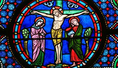A colourful stained glass window depiction of Jesus on the cross