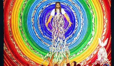A brightly coloured embroidered panel of Jesus, surrounded by concentric circles of rainbow colours, with a crowd of people in front of Him