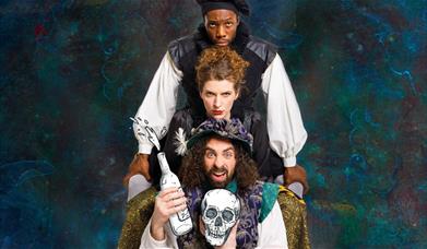 Three members of the cast, holding bottles of wine and the skull of Yorick.