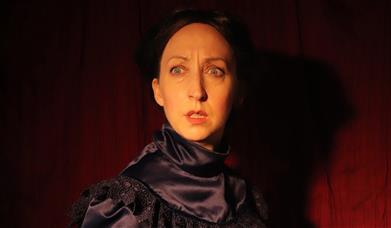 A woman in antique clothing, looks in terror at something off camera.