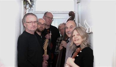 6 people stand in a white small corridor holding string instruments