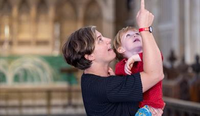Image showing a young child being lifted up by an adult who is pointing to look up high in Bath Abbey.