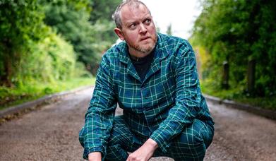 Man in pyjamas squatting down on a  road