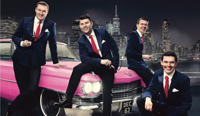The whole band next to a pink Cadillac