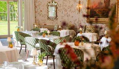 Ornate dining room with decorative wallpaper and chairs, a gold mirror and gold framed painting on the wall. 