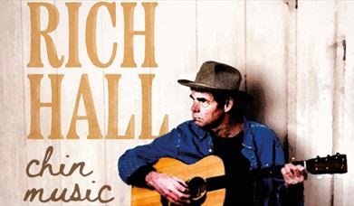 Rich Hall in a cowboy hat, playing an acoustic guitar