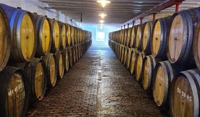 A path between two rows of lambic beer barrels facing each other. The brewery is timmermans and has an original stone floor. At the end of the row the