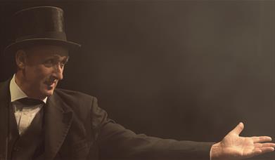 A man in a bowler hat reaches his hand out.