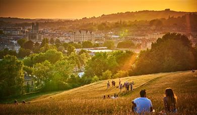Scenic backdrop of people sitting on a hill in the late afternoon/early evening looking down at the city of Bath