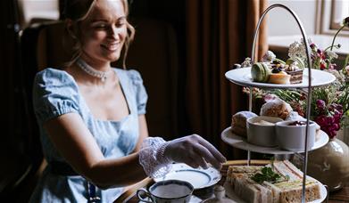 A woman eating afternoon tea while wearing period dress 