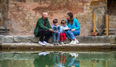 A mother, father and two young sons sitting among some ancient ruins with water in front of them. 