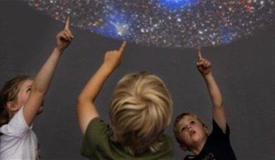 Three children pointing up at a planetarium display 