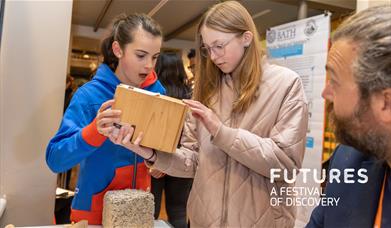 Two young girls study some innovative building materials while a University of Bath researcher explains them