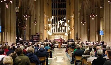 Photo of Chloe Jordan singing Christmas carol to audience sat in chairs inside of Bath Abbey in December as part of Wiltshire and Bath Air Ambulance C