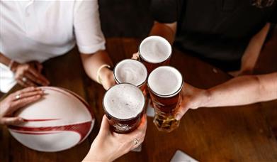 four people cheersing a pint each, with a rugby ball on the table
