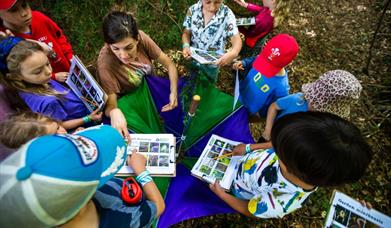 children sitting outside together as adult reads a story book out loud