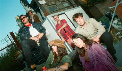 The Band posing on some stairs outside, strong mustaches and a cowboy hat