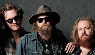 Three men from the band Robert John & The Wreck posing for a photo against a dark background