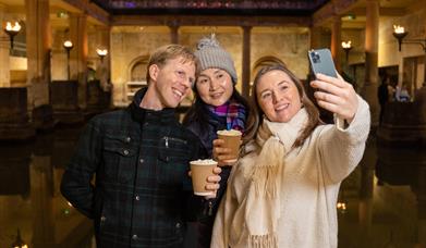 Three visitors enjoying a hot chocolate beside the Great Bath