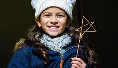young girl holds star made from twigs