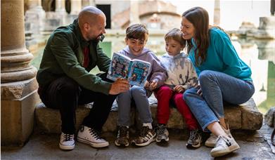 A family sitting beside the Great Bath, looking at a trail sheet