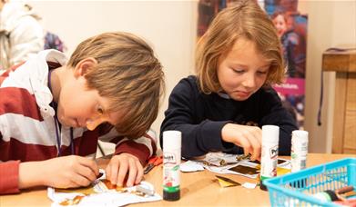 Two boys sitting at a table, working on a cutting and sticking craft activity