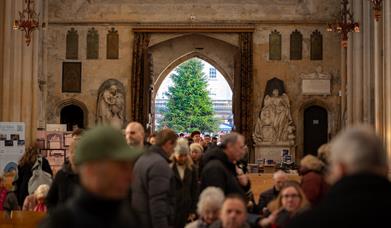 The open doors of a large church showing a Christmas tree outside, while people take their seats for a service inside