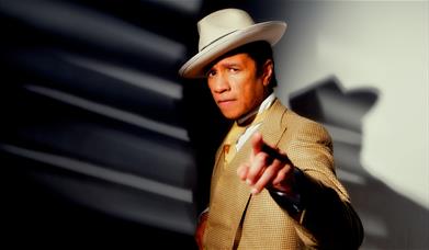 Man in camel suit pointing at the camera.